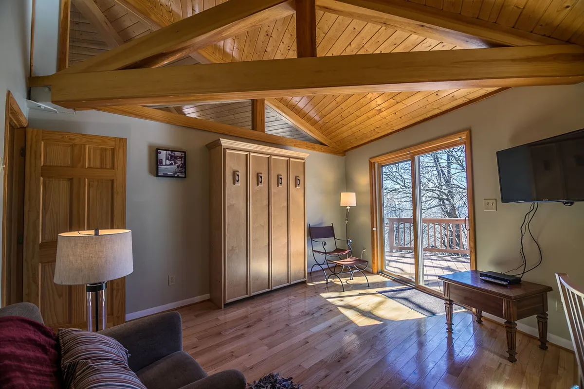 A tranquil seating area with large windows that frame scenic outdoor views. The space is accented by wooden beams and light cabinetry, creating a sense of rustic comfort. The arrangement encourages relaxation, socializing, or quietly enjoying the changing winter landscape.