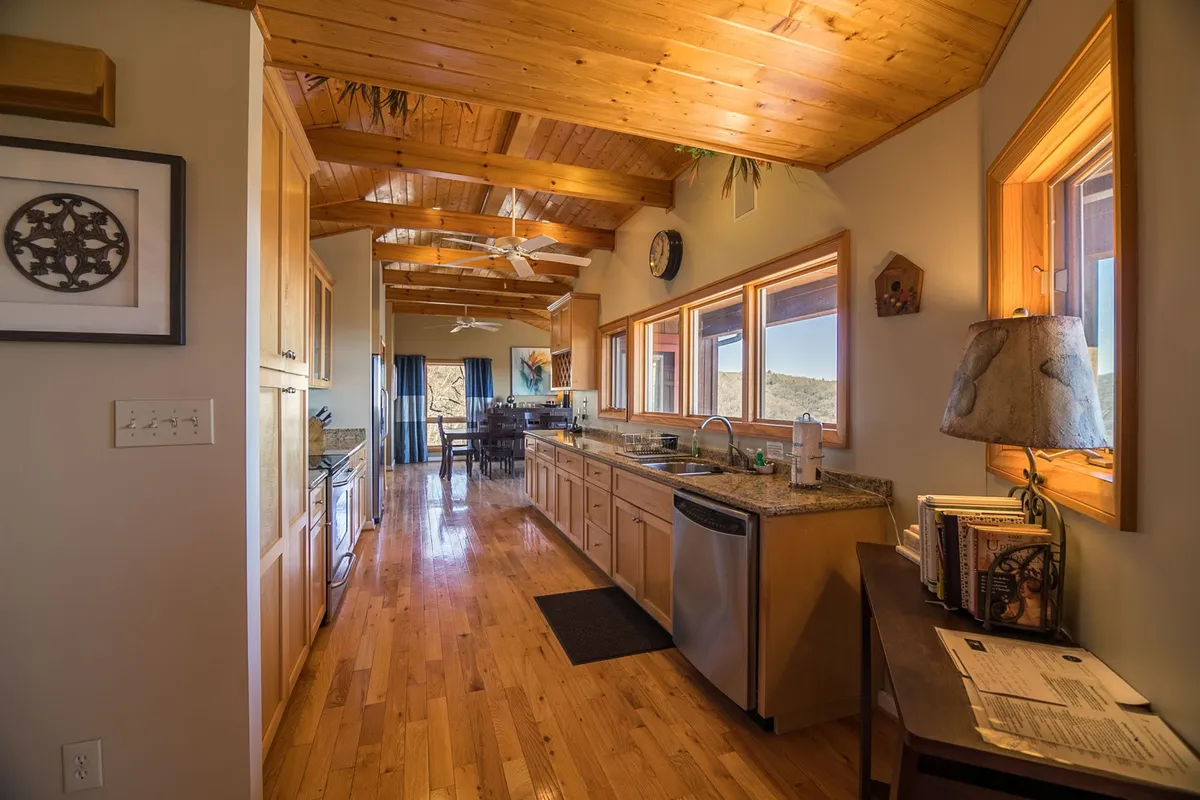 This image showcases the kitchen island set beneath a wooden ceiling, with large windows flooding the space with natural light. The inviting layout hints at easy transitions between indoor comfort and the surrounding outdoors, with ample space for gathering after a day of mountain adventures.