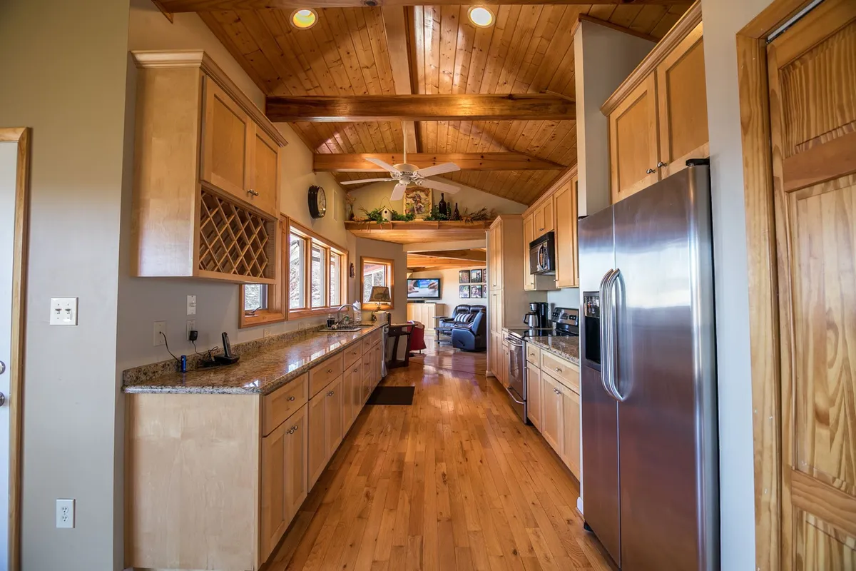 The modern kitchen is showcased with a spacious island, stainless steel appliances, exposed beams, and large windows that bring the mountain scenery indoors. The kitchen is clearly equipped for both casual family breakfasts and celebratory meals.