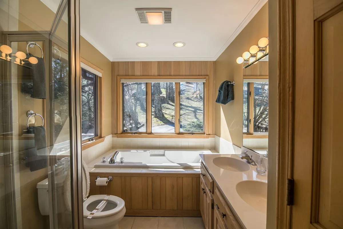 A tranquil bathroom with a prominent bathtub, double sink vanity, and large windows that allow natural light to pour in. The space features wood paneling, creating a spa-like atmosphere perfect for unwinding.